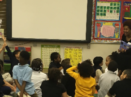 Elementary school students gathered around listening to and discussing a book during the National African American Read-In